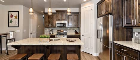 A modern kitchen with dark wood cabinets, stainless steel appliances, and a central island with stools.