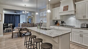 A modern kitchen with a central island, bar stools, and a dining area with a black leather couch.