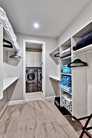 A laundry room with a washing machine, a dryer, and neatly organized shelves with folded towels and blankets.