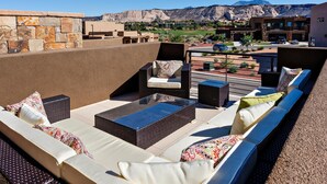 A rooftop terrace with outdoor seating, a stone wall, and a view of a mountainous landscape. - Base Camp (St. George)