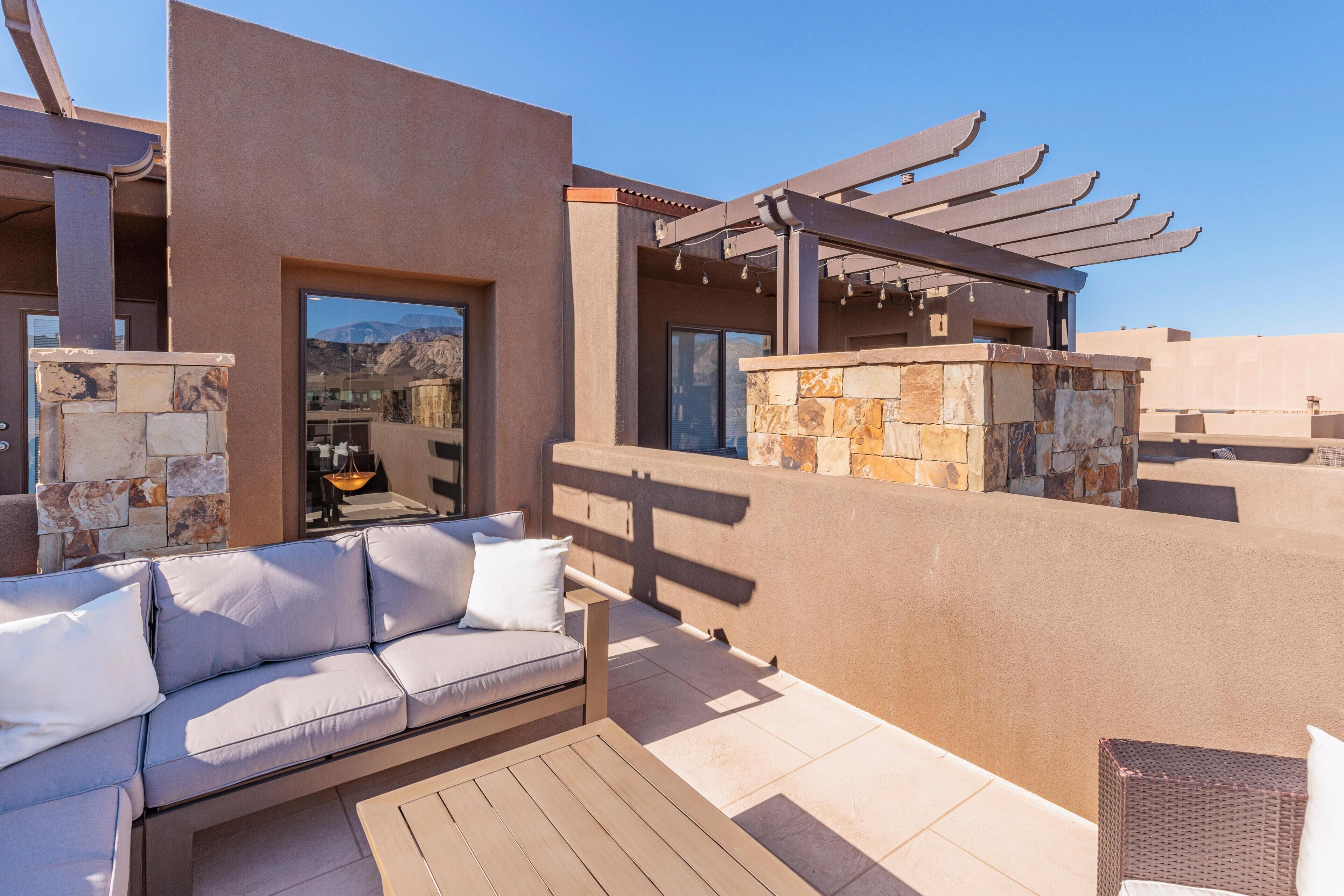 A modern outdoor seating area with a sofa and a table, a pergola with lights, and a stone wall.