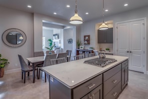 Uma cozinha moderna com uma ilha central, iluminação pendente e um espaço de refeições com cadeiras e uma mesa.