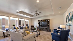 A spacious living room with a large flat-screen TV, comfortable seating, and a ceiling fan. - Fairways Escape (St. George)