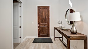 A hallway with a wooden door, a console table with a lamp, and a mirror. - Fairways Escape (St. George)