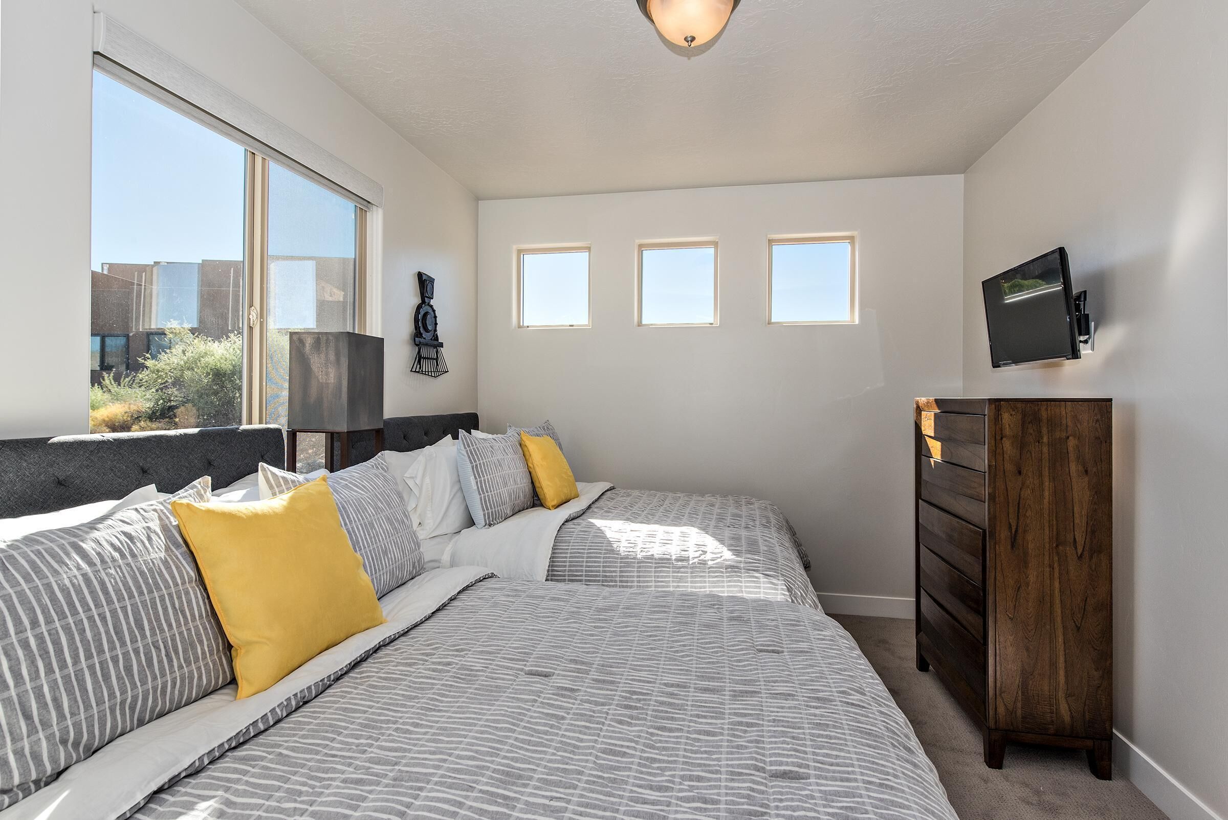 A bedroom with a bed, a dresser, a TV, and three windows.