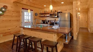 A wooden cabin interior with a kitchen featuring a central island, bar stools, a refrigerator, and a microwave. - Alpine Pool Lodge Holiday home 2 (Pigeon Forge)