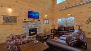 A cozy cabin interior with a stone fireplace, leather sofa, and a television mounted on the wall. - Alpine Pool Lodge Holiday home 2 (Pigeon Forge)