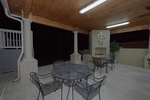 An outdoor patio with a round table and chairs, a brick fireplace, and a wooden ceiling.
