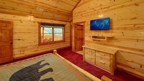 A wooden cabin interior with a ceiling fan, a television mounted on the wall, a window with a view, and a red carpet. - Paradise Point Pool Lodge Holiday home 6 (Sevierville)