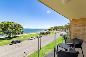 Un balcon aménagé avec du mobilier d’extérieur, donnant sur une rue et une plage.