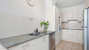 Una cocina moderna con armarios blancos, un lavamanos de acero inoxidable y un reloj en la pared.