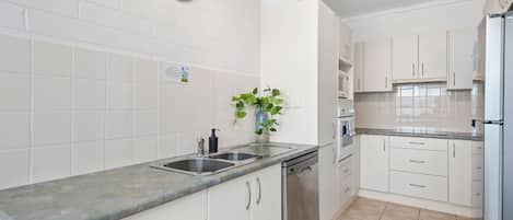 A modern kitchen with white cabinetry, a stainless steel dishwasher, a sink, and a clock on the wall.
