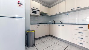A kitchen with white cabinets, a microwave, and a trash bin. - Castaways, 1/17 Shoal Bay Rd - Ground floor, 2-bedroom apartment right across from Shoal Bay Beach (Shoal Bay)