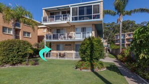 A two-story building with a balcony on the upper floor, surrounded by greenery and a well-maintained lawn. - Castaways, 1/17 Shoal Bay Rd - Ground floor, 2-bedroom apartment right across from Shoal Bay Beach (Shoal Bay)
