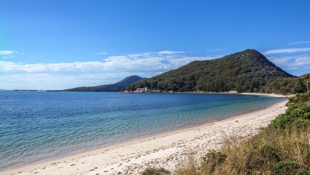 A beach with clear water, a sandy shore, and a mountain in the background. - Castaways, 1/17 Shoal Bay Rd - Ground floor, 2-bedroom apartment right across from Shoal Bay Beach (Shoal Bay)