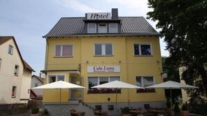 A yellow building with a sign reading "Hotel Cala Luna Restaurant - Hotel" and outdoor seating with umbrellas. - Hotel Restaurant Cala Luna (Marburg)