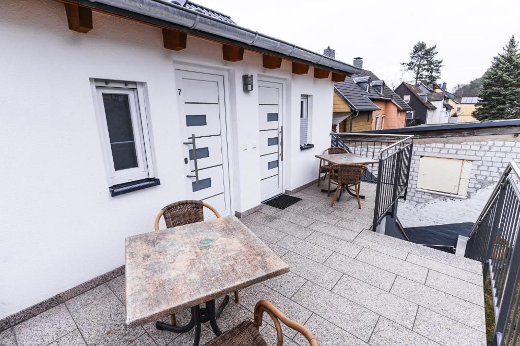 A balcony with a table and chairs, a white building with doors, and a brick wall.