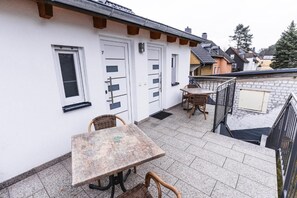 A balcony with a table and chairs, a white building with doors, and a brick wall. - Hotel Restaurant Cala Luna (Marburg)