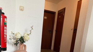 A hallway with wooden flooring, a vase with flowers, and a fire extinguisher on the wall. - Hotel Restaurant Cala Luna (Marburg)