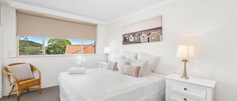 Ein Schlafzimmer mit einem großen Bett, einem Nachttisch, einem Sessel, einem Fenster mit Blick und einem Wandbild.