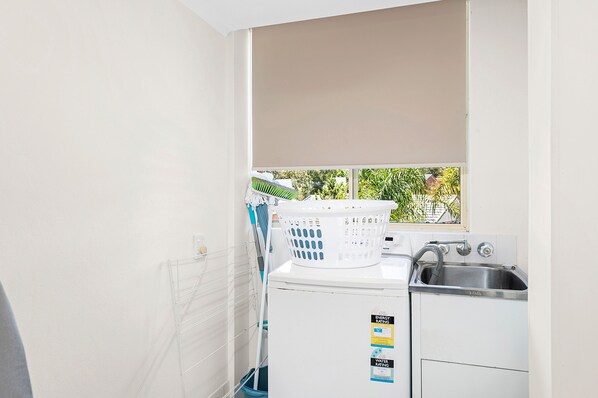 A compact laundry room with a washing machine, a drying rack, and a window with a view of greenery.