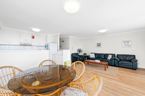 A modern living room with a dining area, a black leather sofa, and a white kitchen with white cabinets. - Seaspray 3 close to Shoal Bay Beach (Nelson Bay)