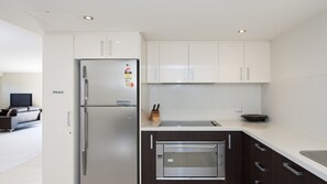 A modern kitchen with white cabinets, a stainless steel refrigerator, and a built-in oven. - Dolphin Cove Apartments, 13/2-6 Nelson Bay - 300m stroll to the marina! (Nelson Bay)