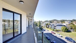 A modern hotel balcony with large windows offering a view of a cityscape and a road. - Dolphin Cove Apartments, 13/2-6 Nelson Bay - 300m stroll to the marina! (Nelson Bay)