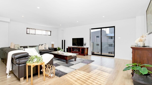 A modern living room with a sofa, coffee table, and TV. There is a sliding glass door leading to a balcony. - Dolphin Cove Apartments, 13/2-6 Nelson Bay - 300m stroll to the marina! (Nelson Bay)