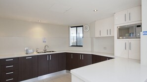 A modern kitchen with dark cabinets, white countertops, a stainless steel sink, and a built-in microwave. - Dolphin Cove Apartments, 13/2-6 Nelson Bay - 300m stroll to the marina! (Nelson Bay)