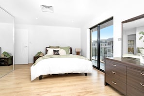 Een moderne slaapkamer met een groot bed, een dressoir, een spiegel en uitzicht op de stad door een glazen deur.