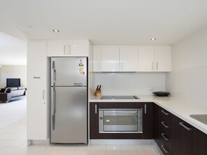 A modern kitchen with a stainless steel refrigerator, a built-in oven, and white cabinetry. - Dolphin Cove 13 Luxury Apartment in Nelson Bay (Nelson Bay)
