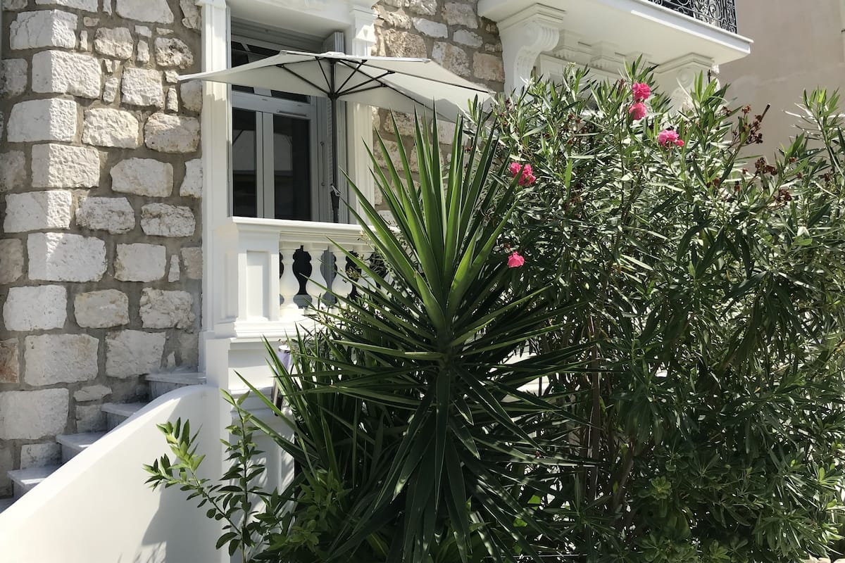 A stone building with a white balcony and a large plant with pink flowers.