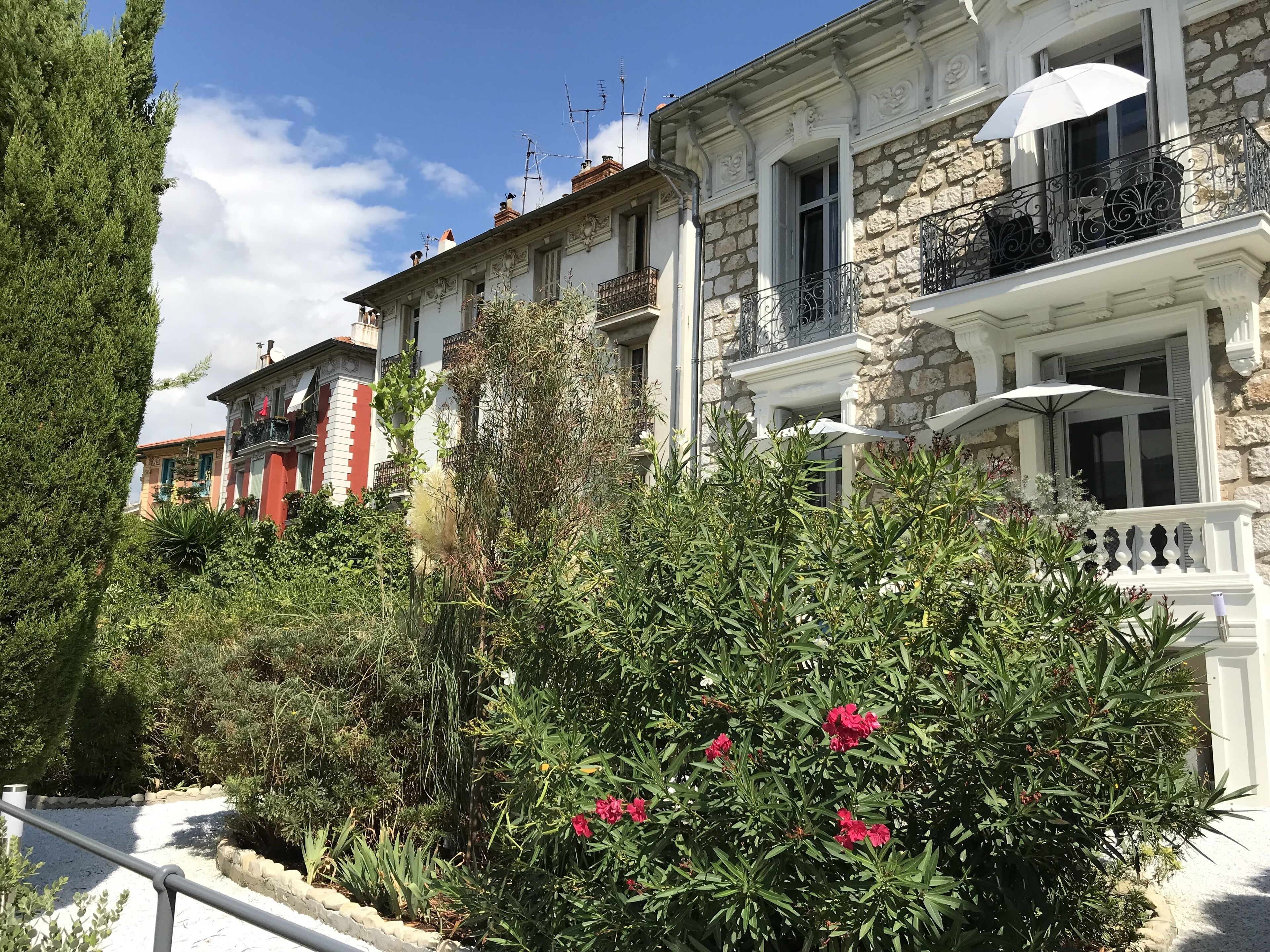 Une rangée de bâtiments traditionnels en pierre, dotés de balcons, entourée d’une végétation luxuriante et de plantes en fleurs.