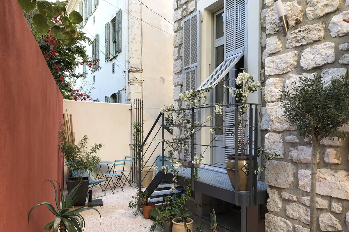 A narrow courtyard with a stone wall, a staircase, and various potted plants.