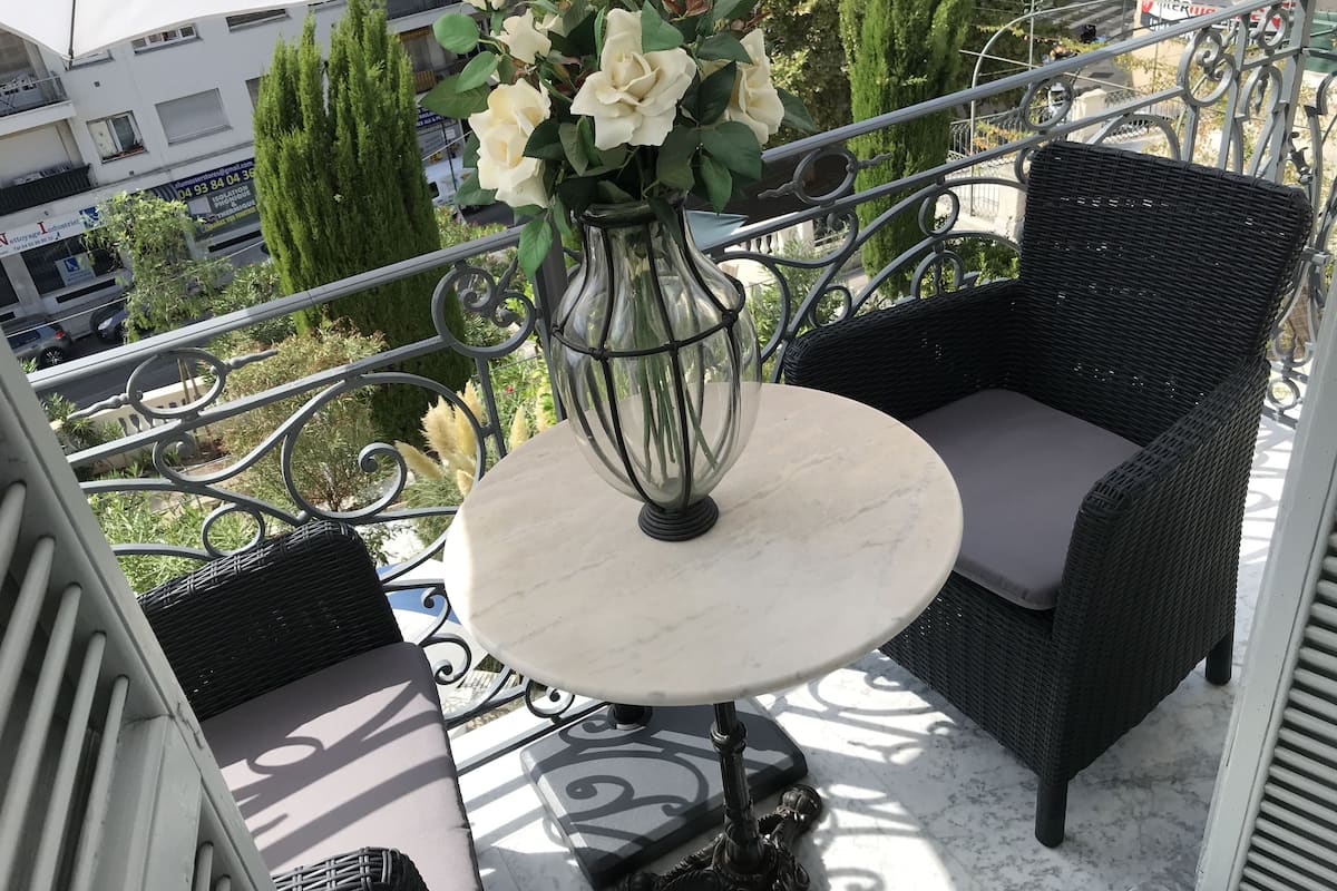 A balcony with wicker furniture, a round table with a vase of flowers, and a view of the cityscape.