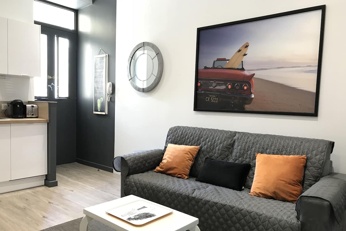 A modern living room with a grey quilted sofa, a white coffee table, and a framed picture of a vintage car on the wall.