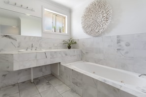 Ein modernes Badezimmer mit Marmorwaschbecken, einer großzügigen Badewanne und einer dekorativen Wandgestaltung.
