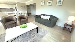 A living room with a sofa, two armchairs, a coffee table, and a lamp. - Misthaven Nelson Bay Apartment with Views (Nelson Bay)
