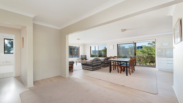 A spacious living area with a dining table and sofas, large windows, and a view of the outdoors.