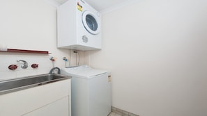 A compact laundry area with a washing machine, a sink, and a faucet. - Misthaven Nelson Bay Apartment with Views (Nelson Bay)