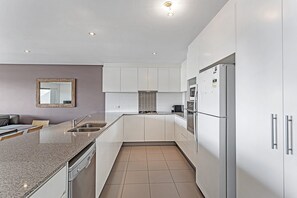 A modern kitchen with white cabinetry, a granite countertop, and a built-in dishwasher. - Surfside 5 Fingal Bay Apartment with Water Views (Fingal Bay)