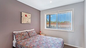 A bedroom with a bed, a window with a view, and a wall-mounted artwork.