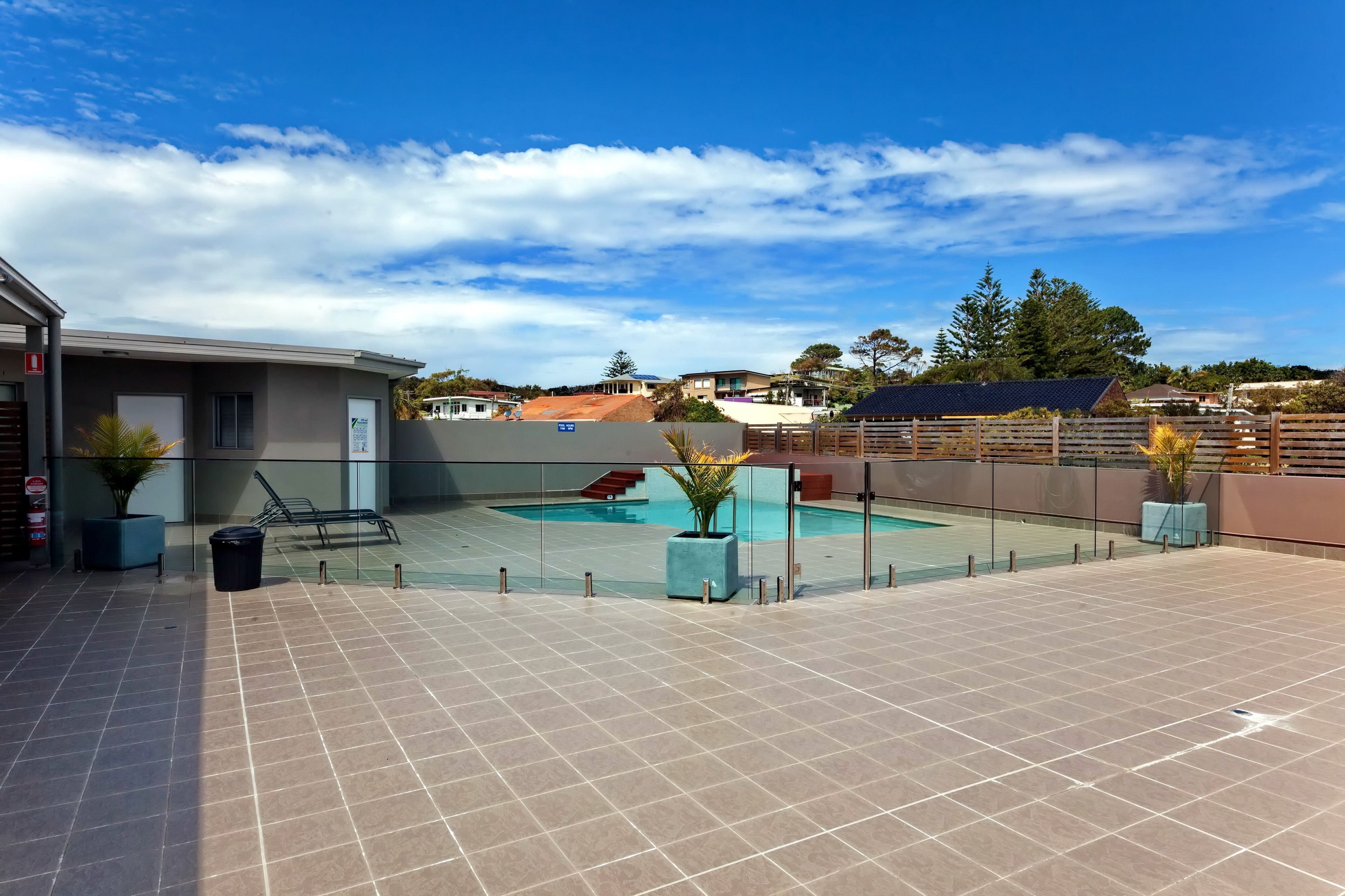 Un área de piscina en la azotea con cielo despejado, un edificio con un letrero y una piscina cercada.