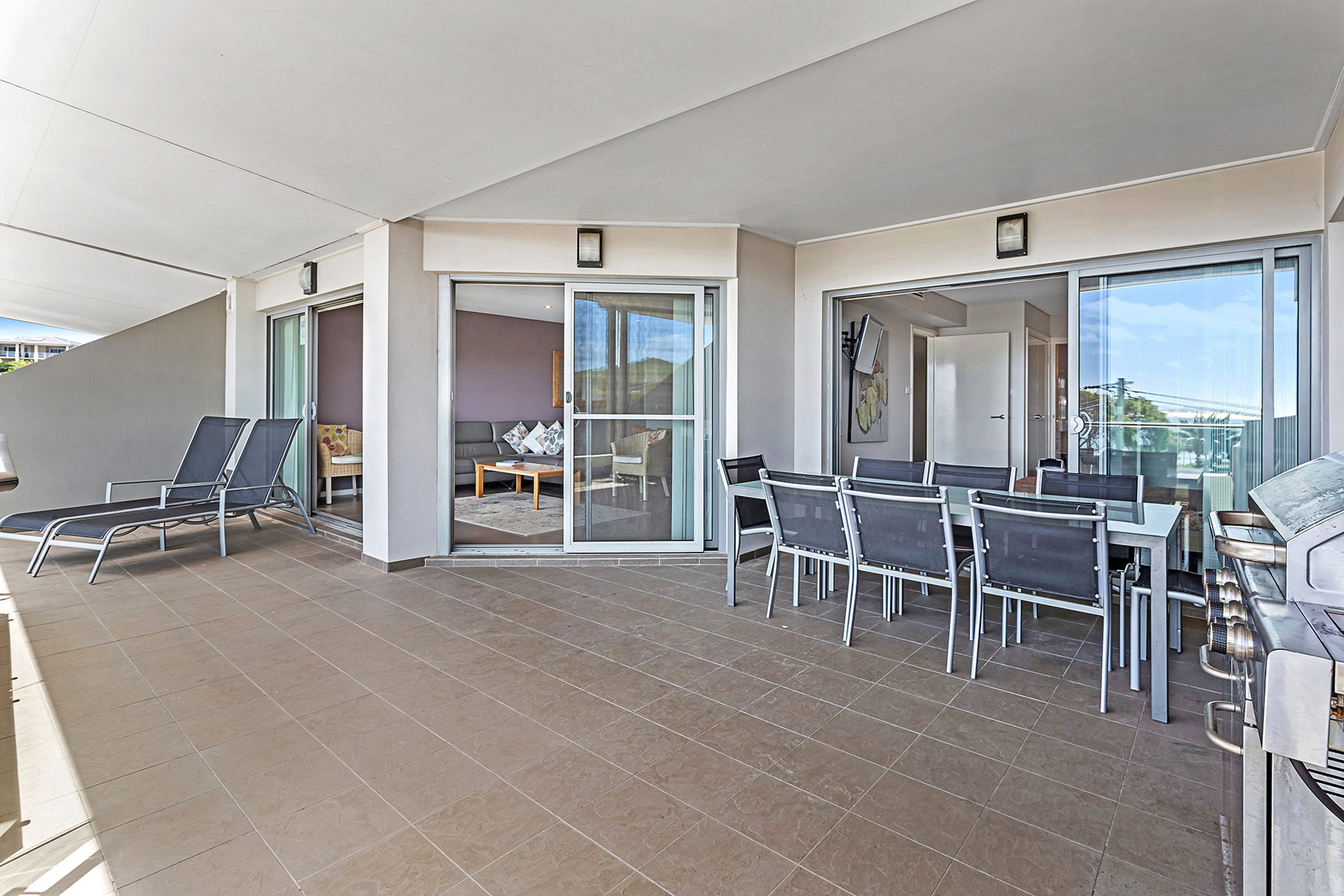 Un balcon doté d’un espace salon, d’un barbecue et d’une porte-fenêtre coulissante donnant accès à un espace intérieur.