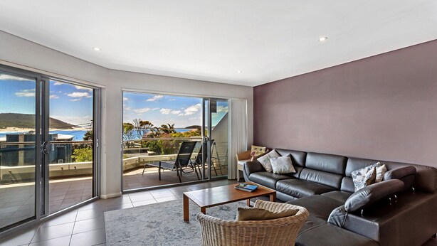A modern living room with a large sliding glass door leading to a balcony with a view of the beach and ocean.
