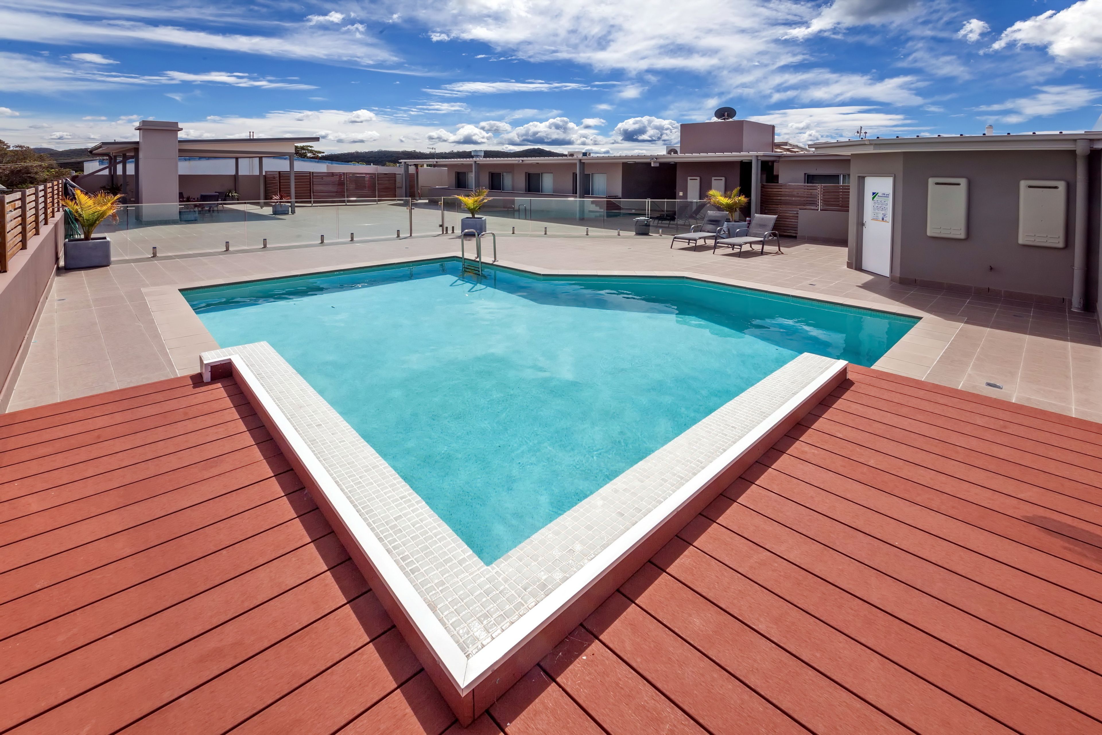 A rectangular swimming pool with a tiled edge, surrounded by a wooden deck.