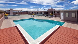 Piscina retangular com borda revestida e deck de madeira ao redor.