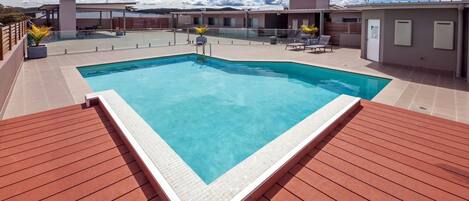 A rectangular swimming pool with a tiled edge, surrounded by a wooden deck.
