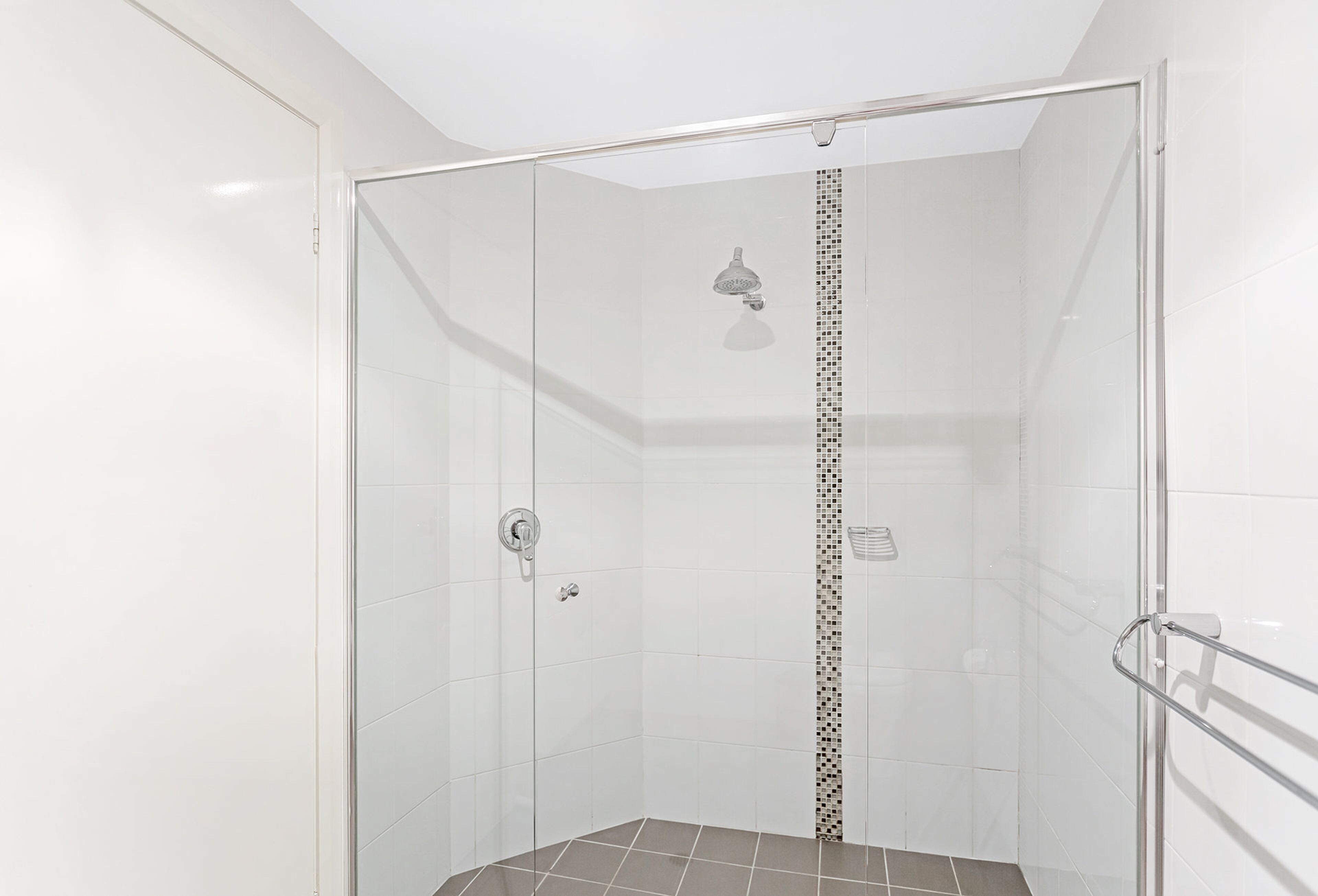 A glass-enclosed shower stall with a showerhead, a control knob, and a tiled floor.